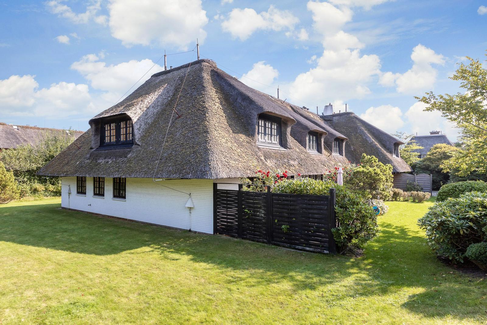 Haus mit strohgedecktem Dach und weißer Fassade im Garten