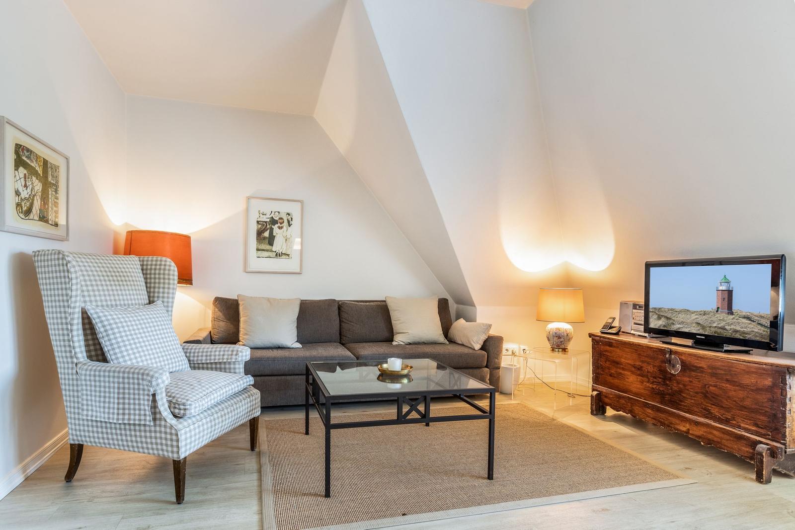 Wohnzimmer mit Sofa, Sessel, Couchtisch und Fernseher auf Holzschrank.