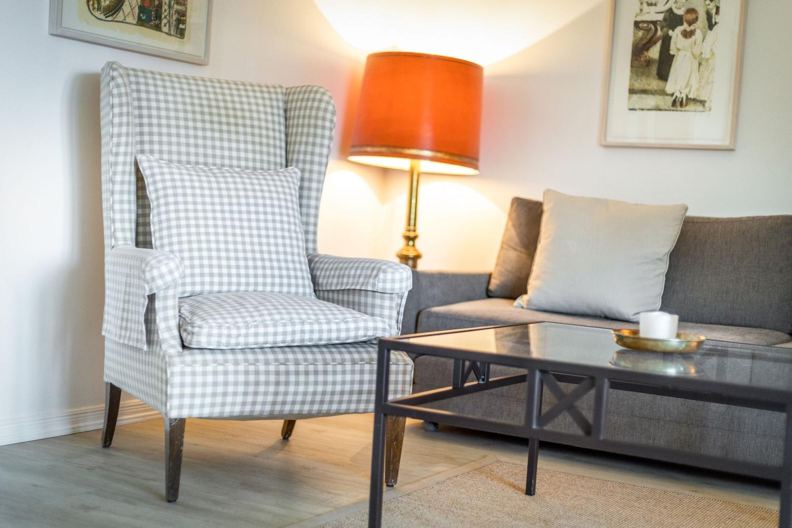 Ein Sessel mit kariertem Stoff und ein Sofa mit Kissen stehen vor einem Couchtisch.