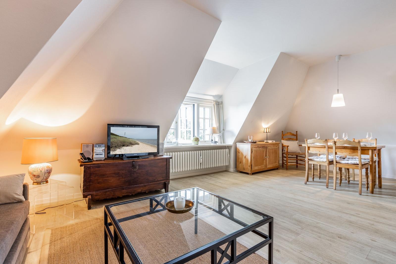 Wohn- und Essbereich mit Holzboden, TV, Tisch und Stühlen unter schrägen Dachdecken.