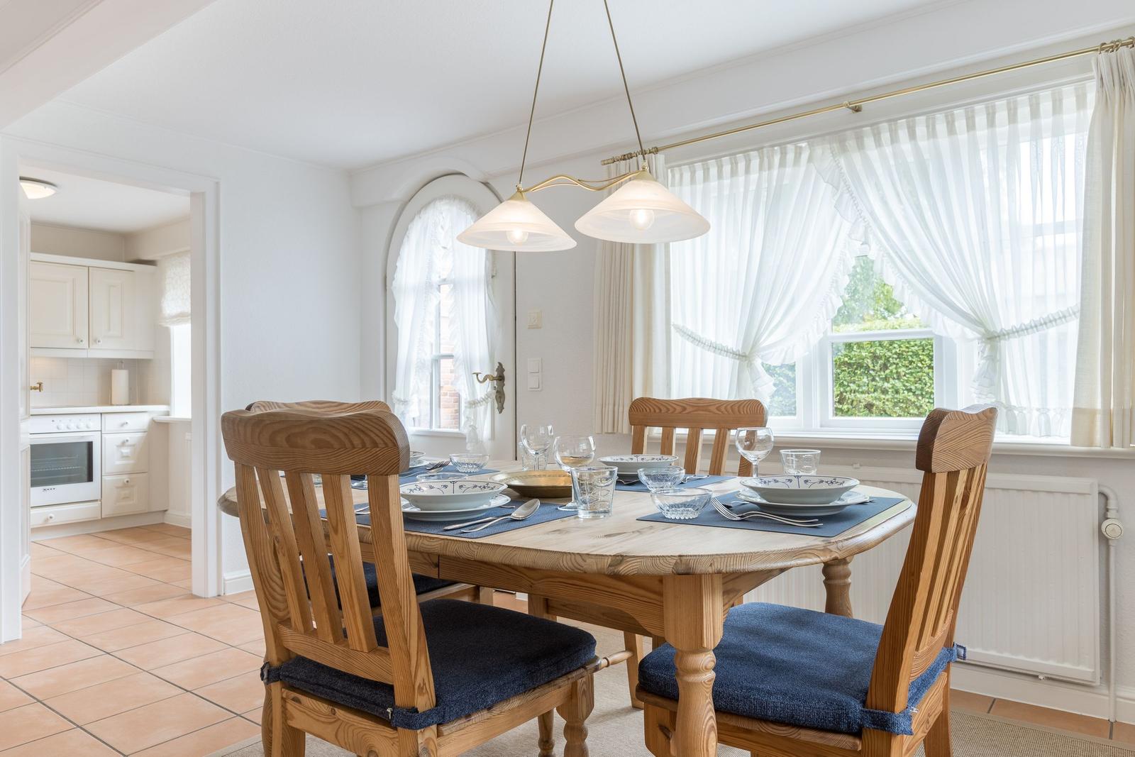 Esszimmer mit Holztisch, Stühlen und Fenster mit weißen Vorhängen.
