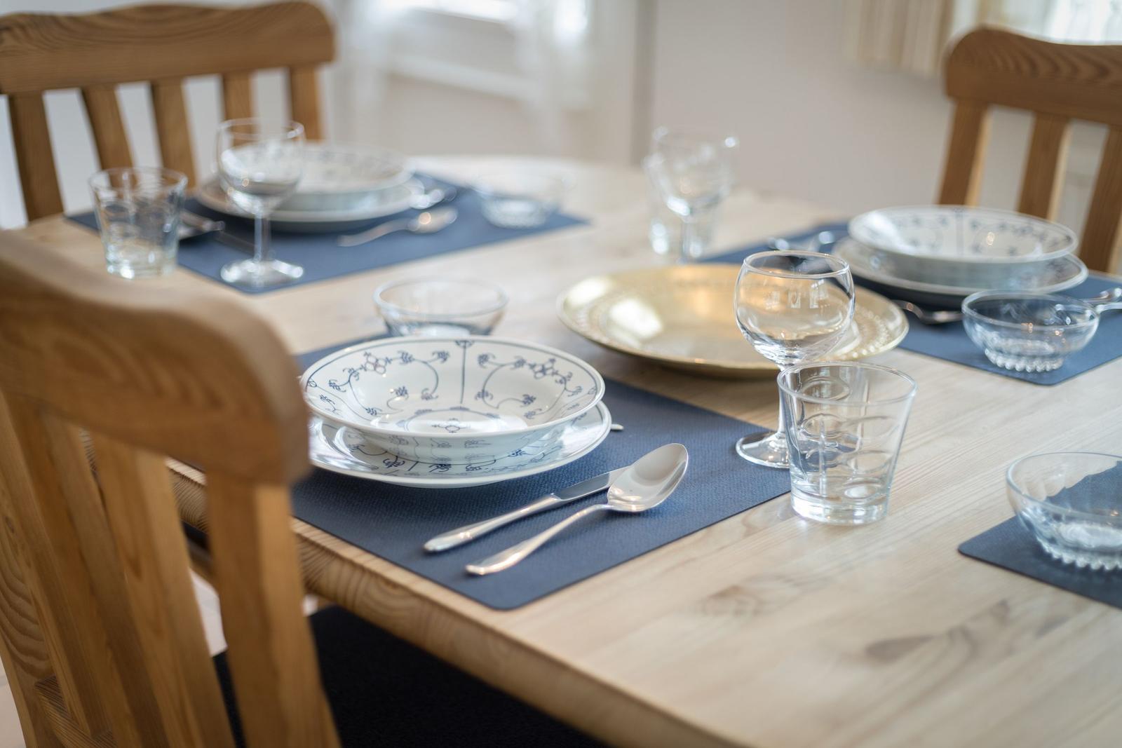 Holztisch mit blauen Platzsets und Geschirr für vier Personen.