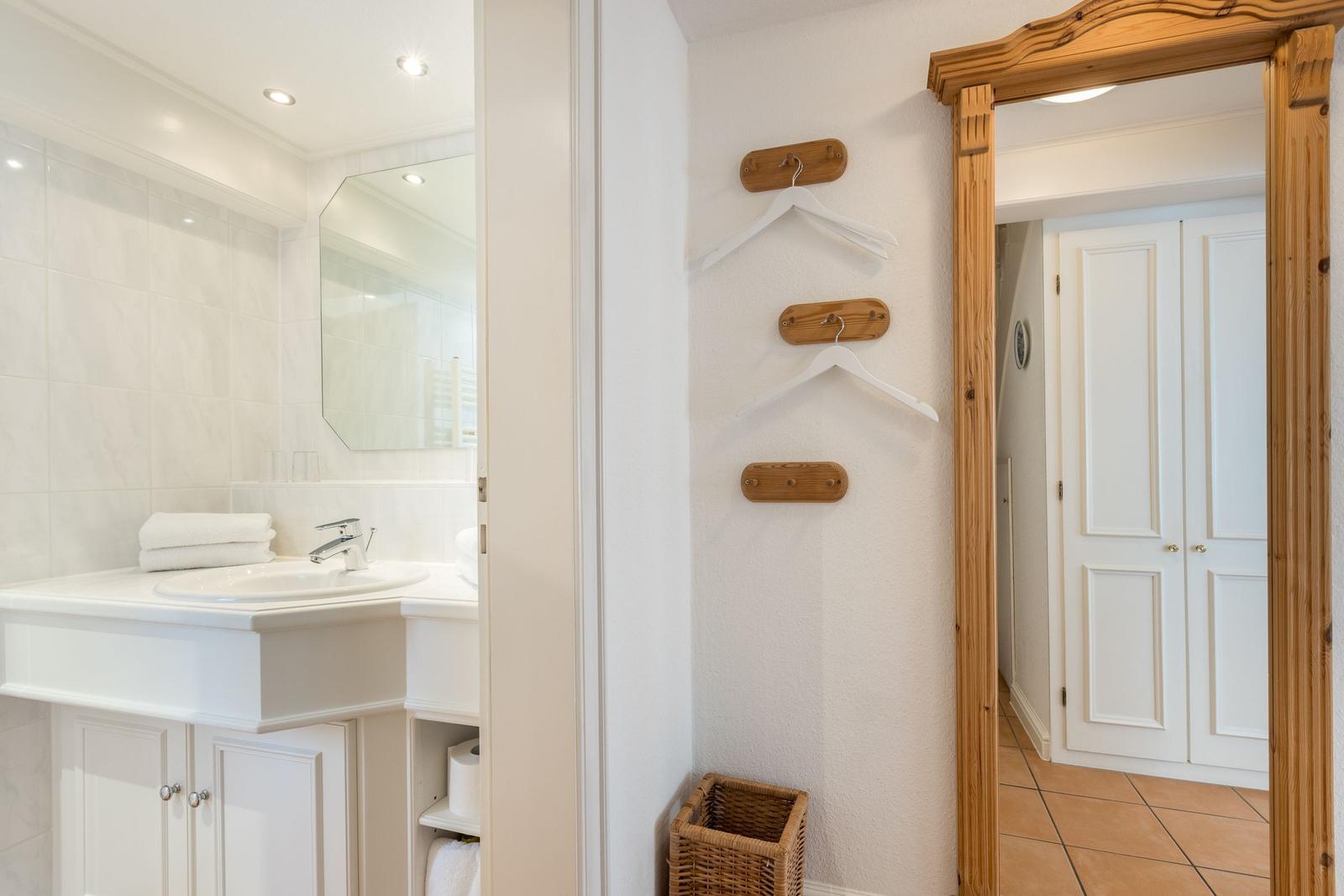 Badezimmer mit Waschbecken und Spiegel. Wand mit Haken und Korb.