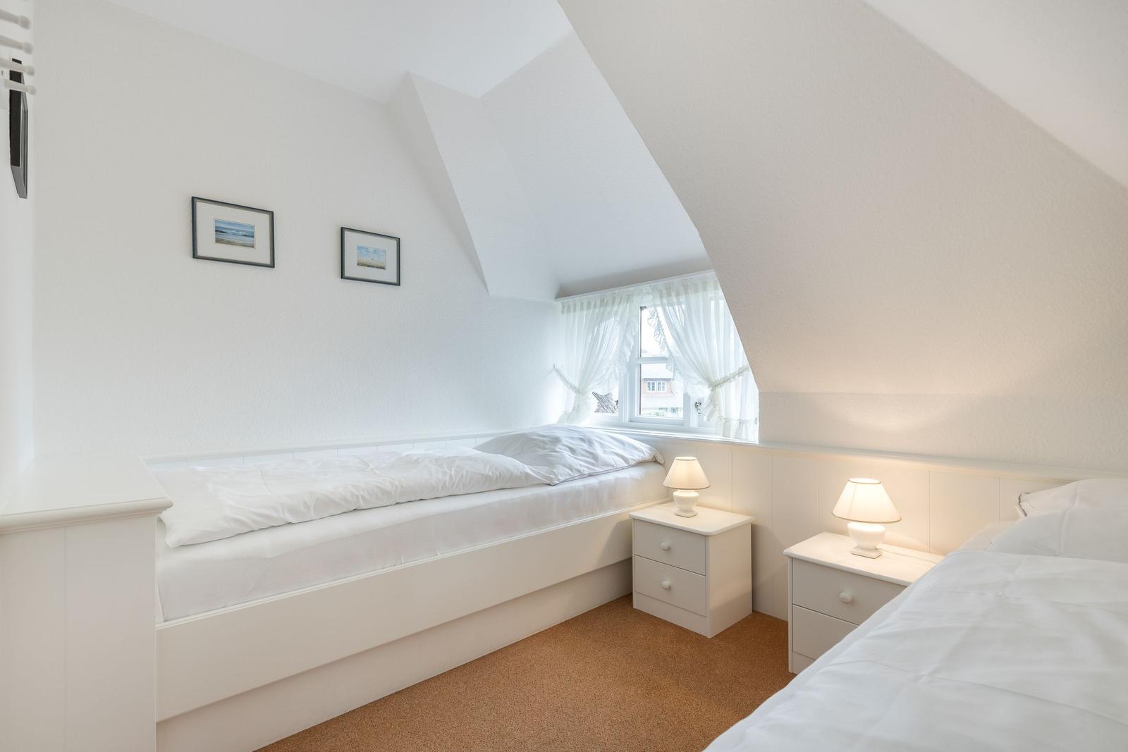 Zimmer mit zwei Betten, Fenster und Nachttischen unter Dachschrägen.