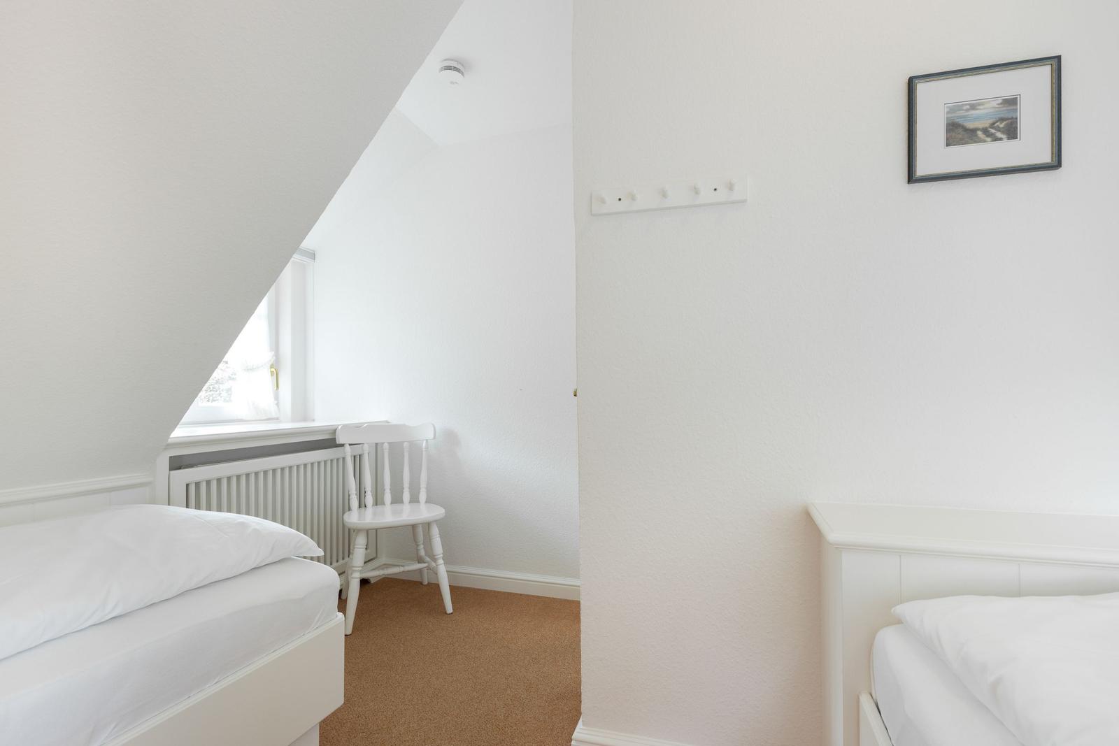 Zimmer mit zwei Betten, weißer Stuhl und Fenster unter Dachschräge.