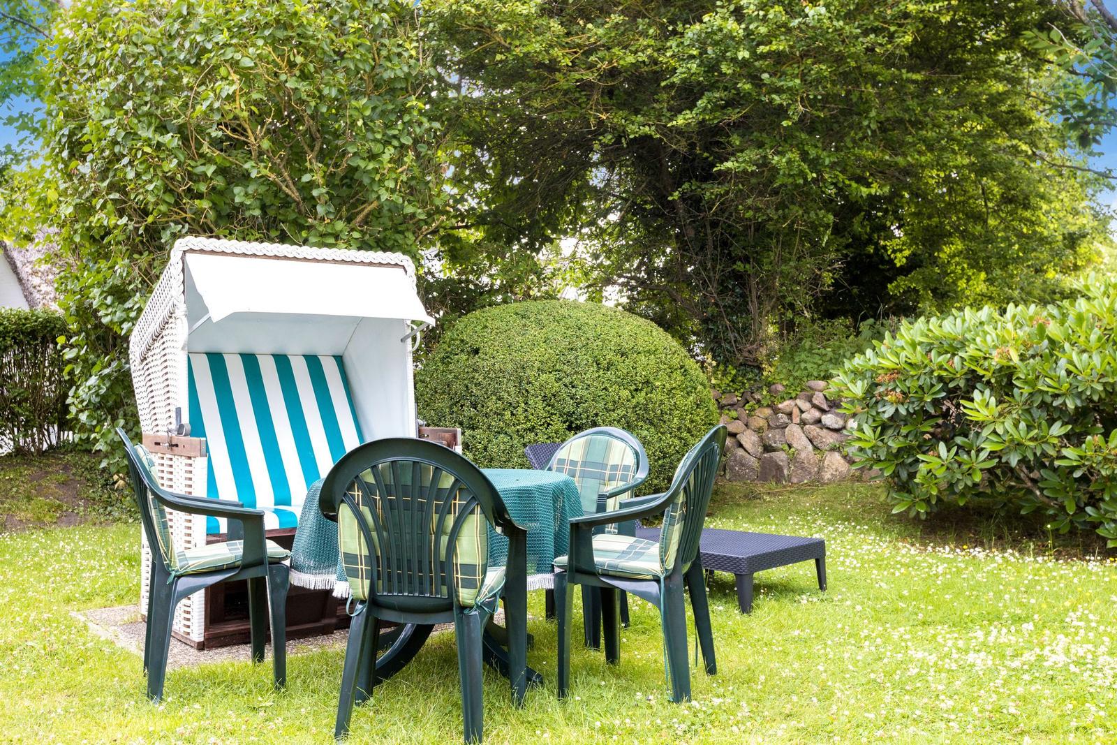 Garten mit Liegestuhl, Tisch und Stühlen. Grünflächen und Sträucher umgeben den Bereich.