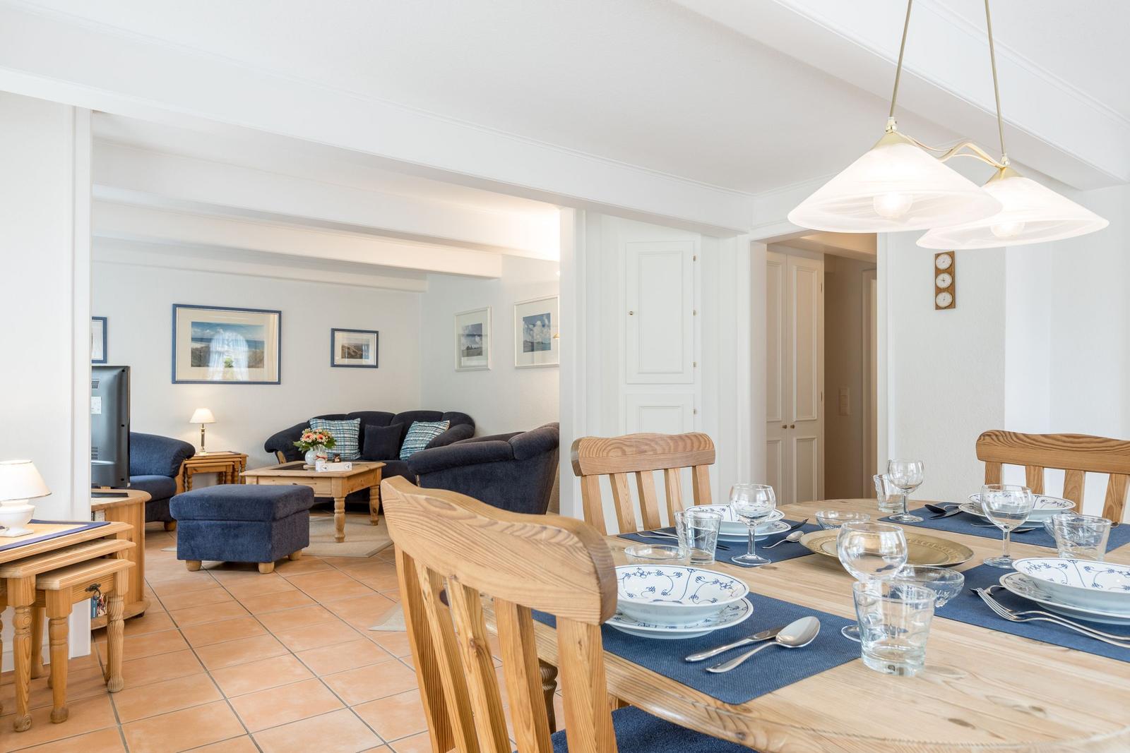 Esszimmer mit Holztisch und Stühlen, Wohnzimmer im Hintergrund mit Sofa und Fernseher.
