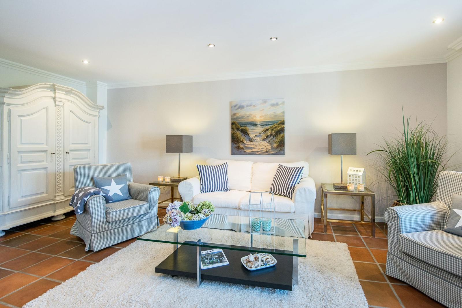 Wohnzimmer mit Sofa, zwei Sesseln, Glas-Tisch und Wandbild