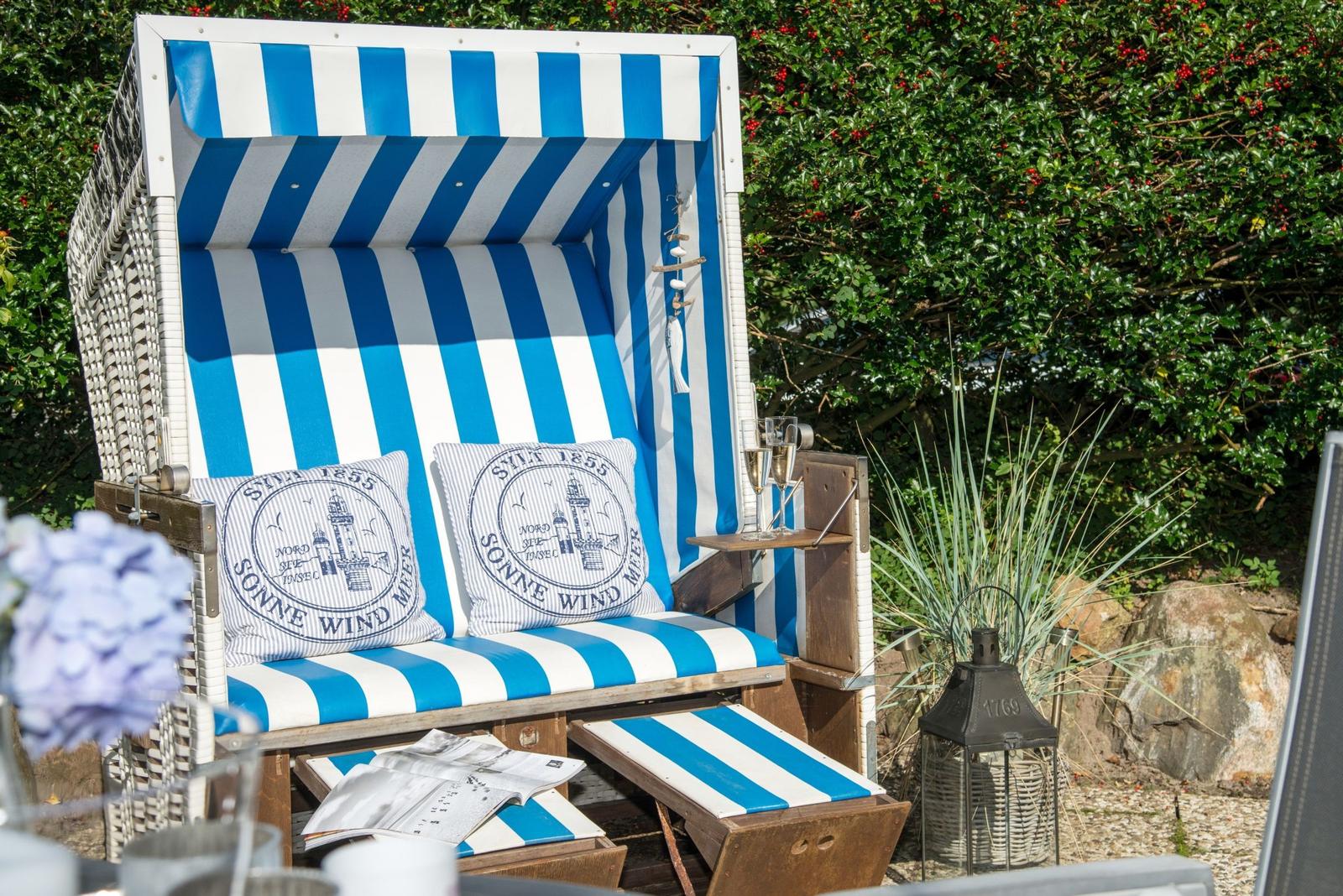 Blau-weiße Strandliege mit Kissen und Getränken im Garten.
