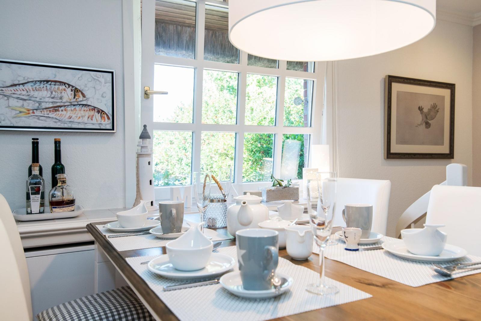 Esstisch mit Tassen, Gläsern und Dekoration an Fenster