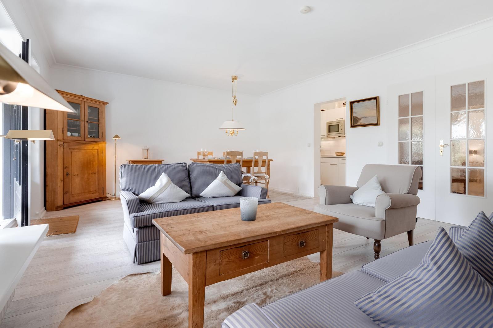 Wohnzimmer mit Sofa, Sessel und Holztisch. Küche und Essbereich im Hintergrund.