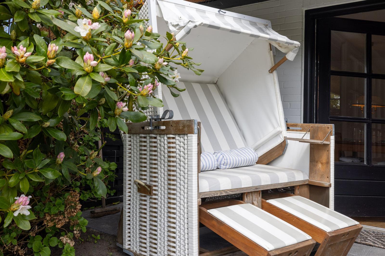 Strandkorb mit Streifenbezug und Kissen vor einem Haus mit Blumen