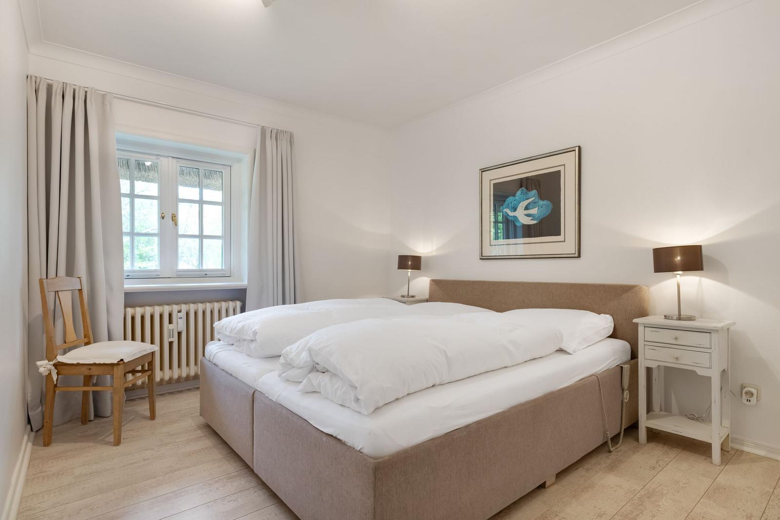 Schlafzimmer mit Bett, Nachttisch und Fenster.