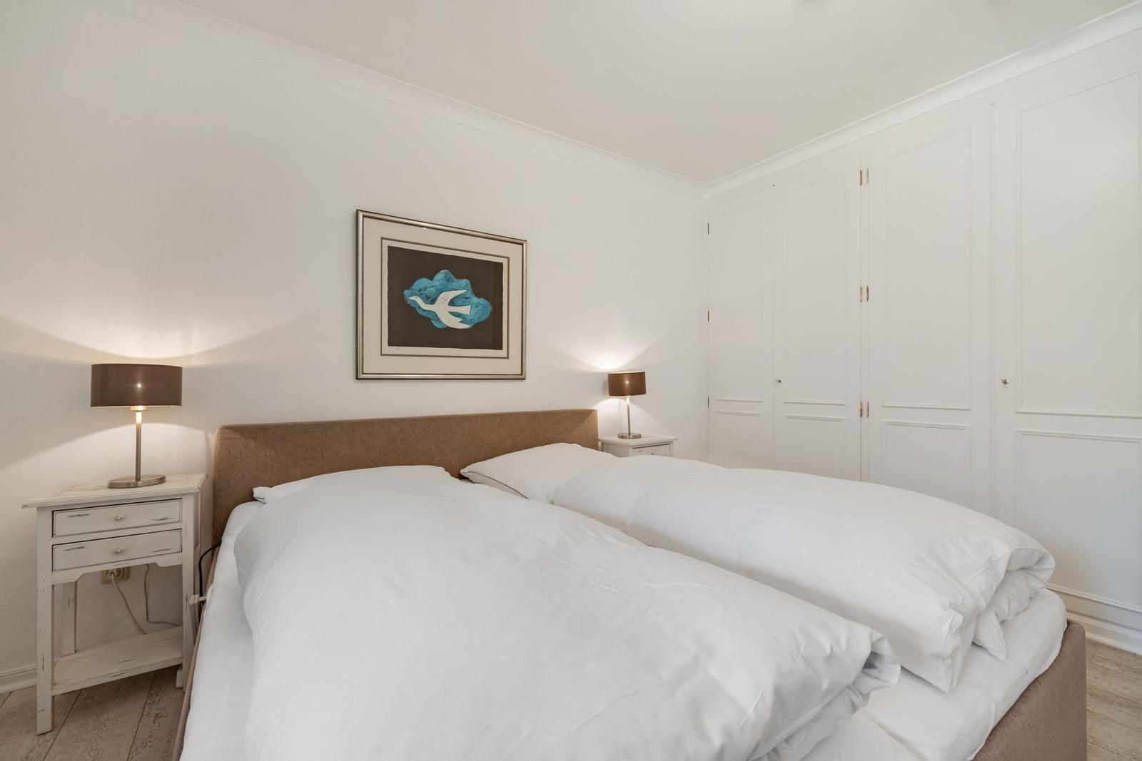 Schlafzimmer mit Doppelbett, Nachttischen und weißen Schränken.