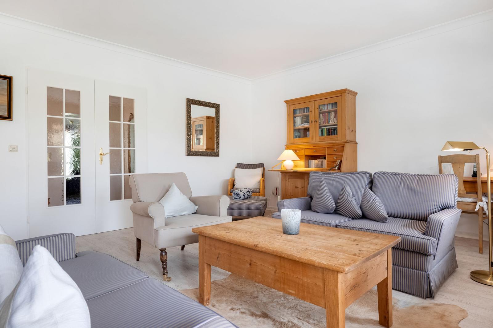Wohnzimmer mit Sofa, Sessel und Holztisch. Bücherregal und Tür mit Glasfenstern.