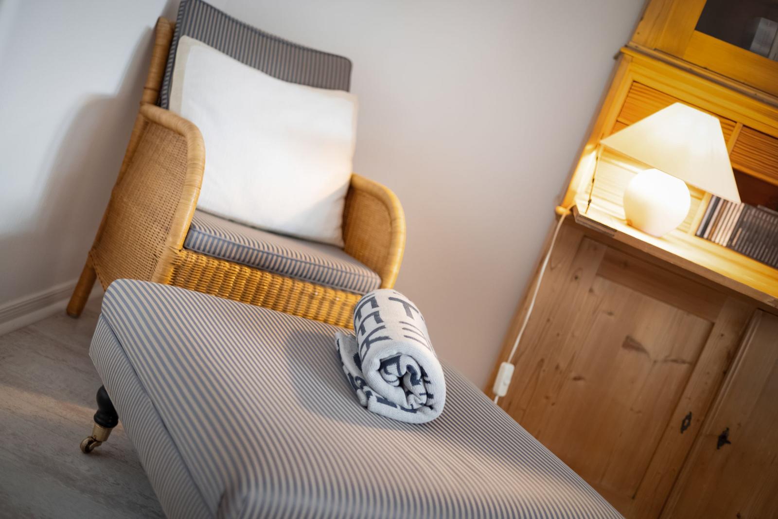 Rattan-Stuhl mit Kissen und gestreifter Auflage. Holzschrank mit Lampe und Handtuch.