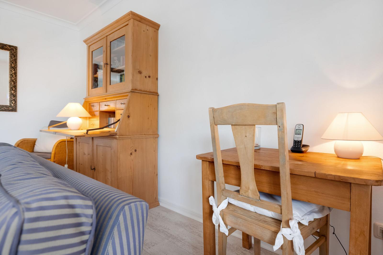 Holzschreibtisch mit Stuhl, Lampe und Telefon. Hintergrund: Holzschrank und Sofa mit Streifen.