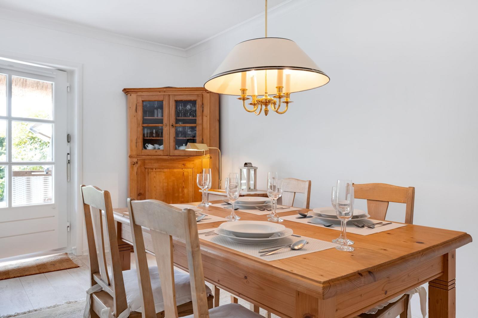 Esszimmer mit Holztisch, Stühlen und Glasgarnitur. Hängelampe und Holzschrank sichtbar.