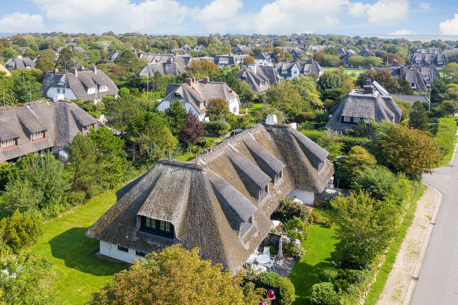 Dorf mit strohgedeckten Häusern und grünen Gärten unter blauem Himmel.