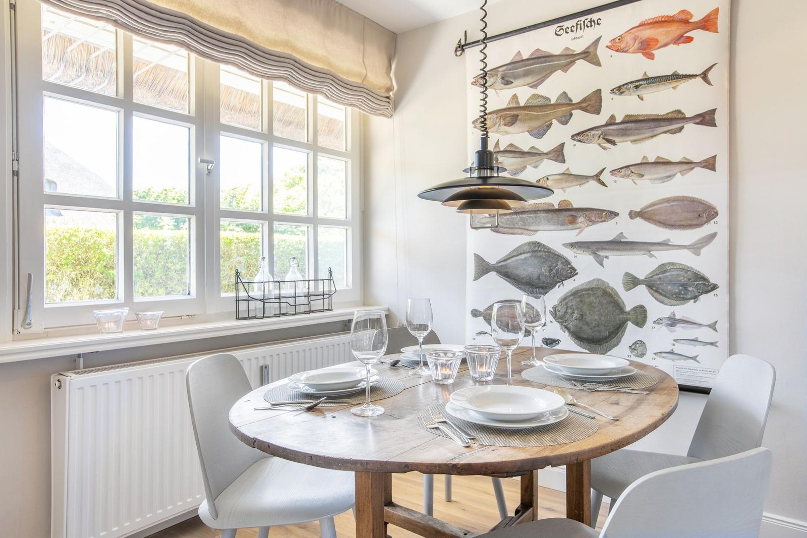 Rundtisch mit Stühlen, Wandbild mit Fischen, Fenster mit Blick auf Grün.