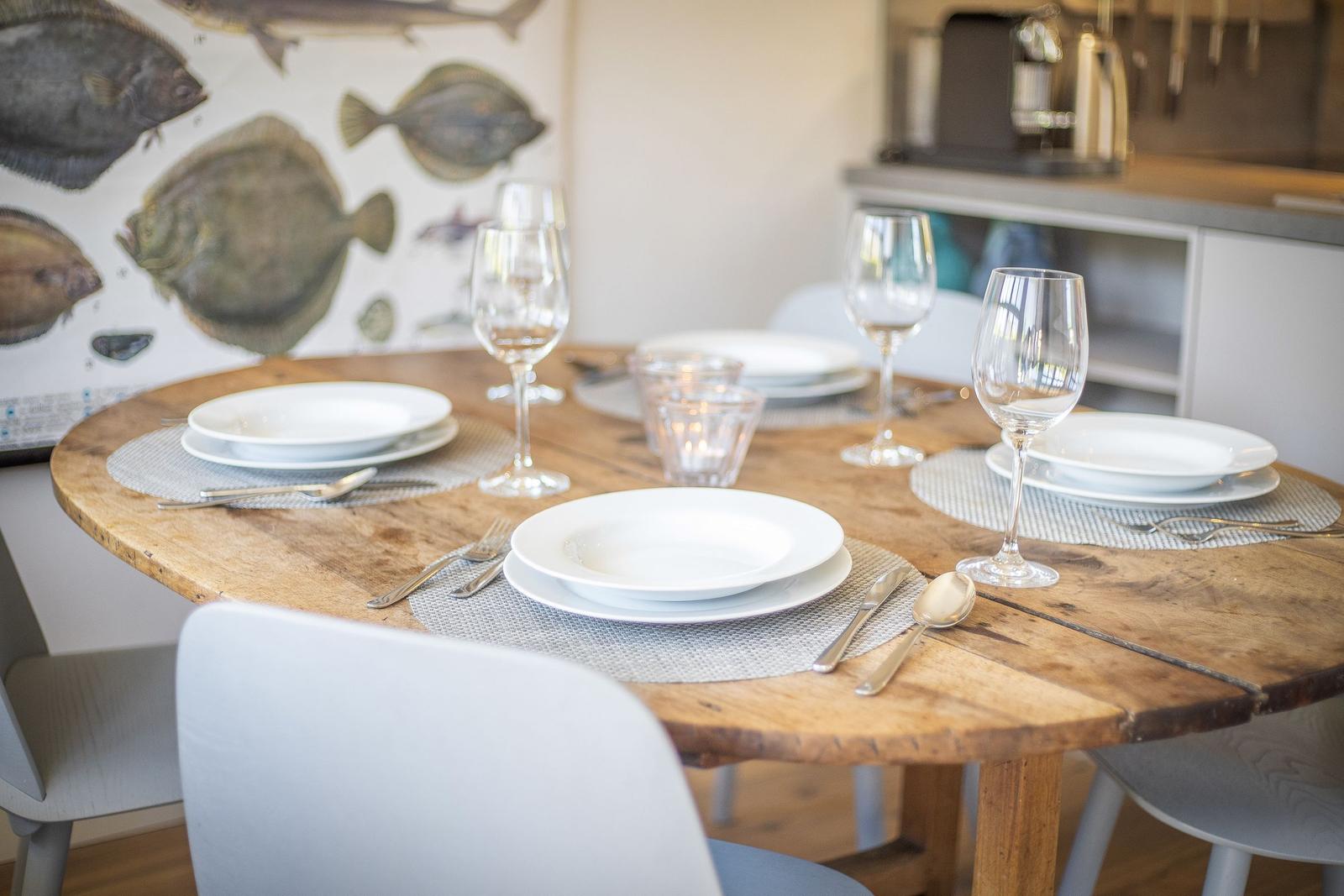 Runder Holztisch mit Tischdecken und Geschirr. Wandbild mit Fischen im Hintergrund.