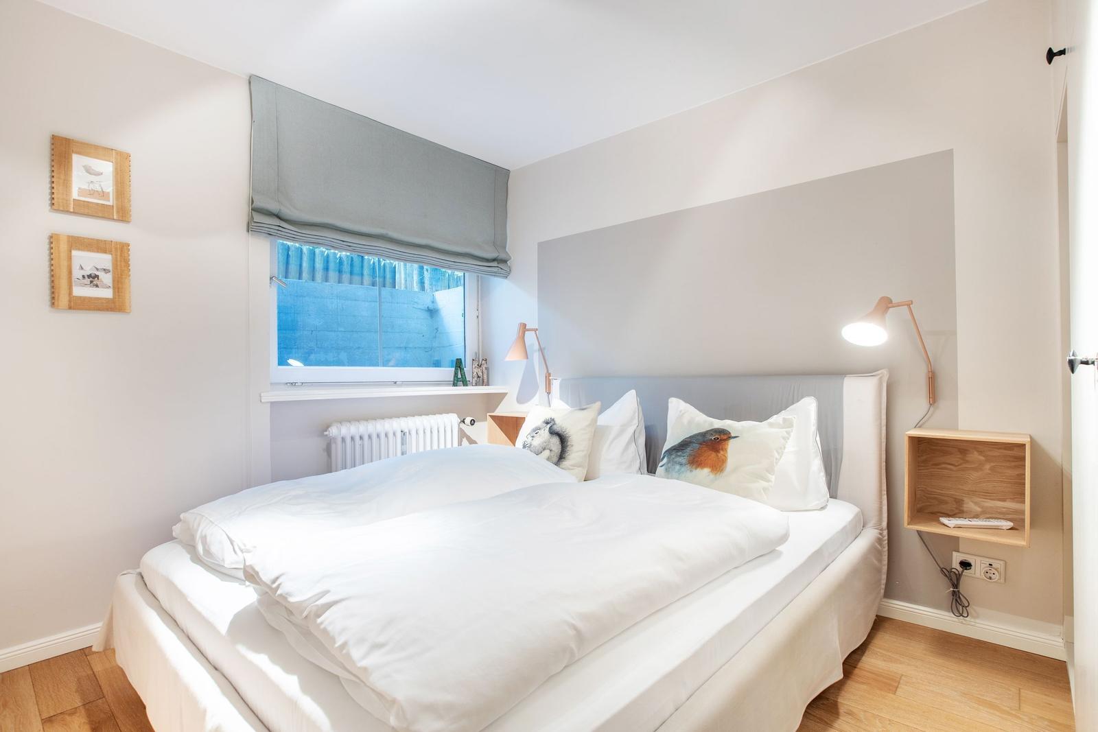 Schlafzimmer mit weißem Bett, Fenster und Holzboden.