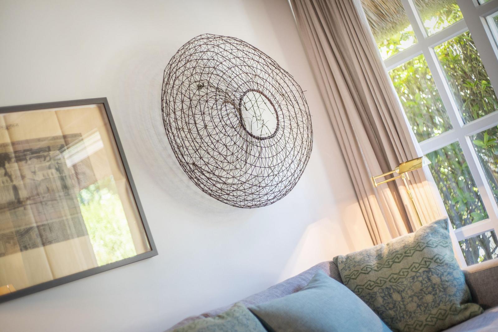 Wanddekoration mit Drahtkunstwerk, Fenster mit Vorhängen und Kissen auf Sofa