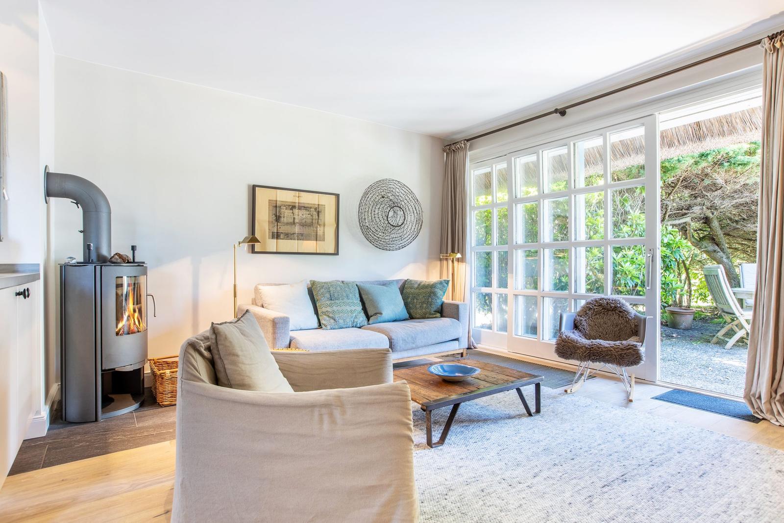 Wohnzimmer mit Sofa, Kamin und Glastür zum Garten