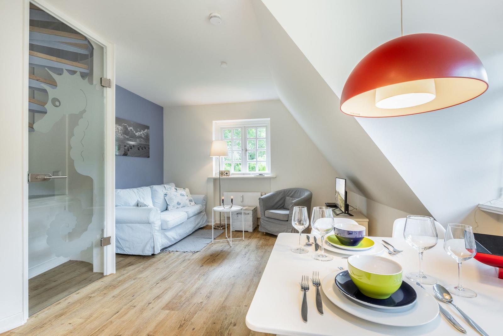 Dining room with table set for four, red pendant light, and view into living area with sofa and window.
