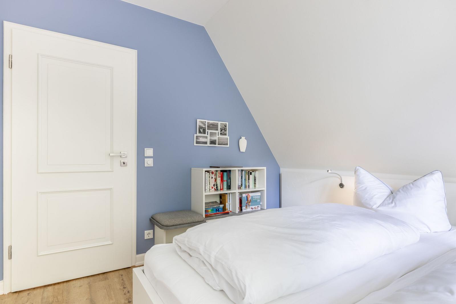 Schlafzimmer mit Bett, Bücherregal und Tür.