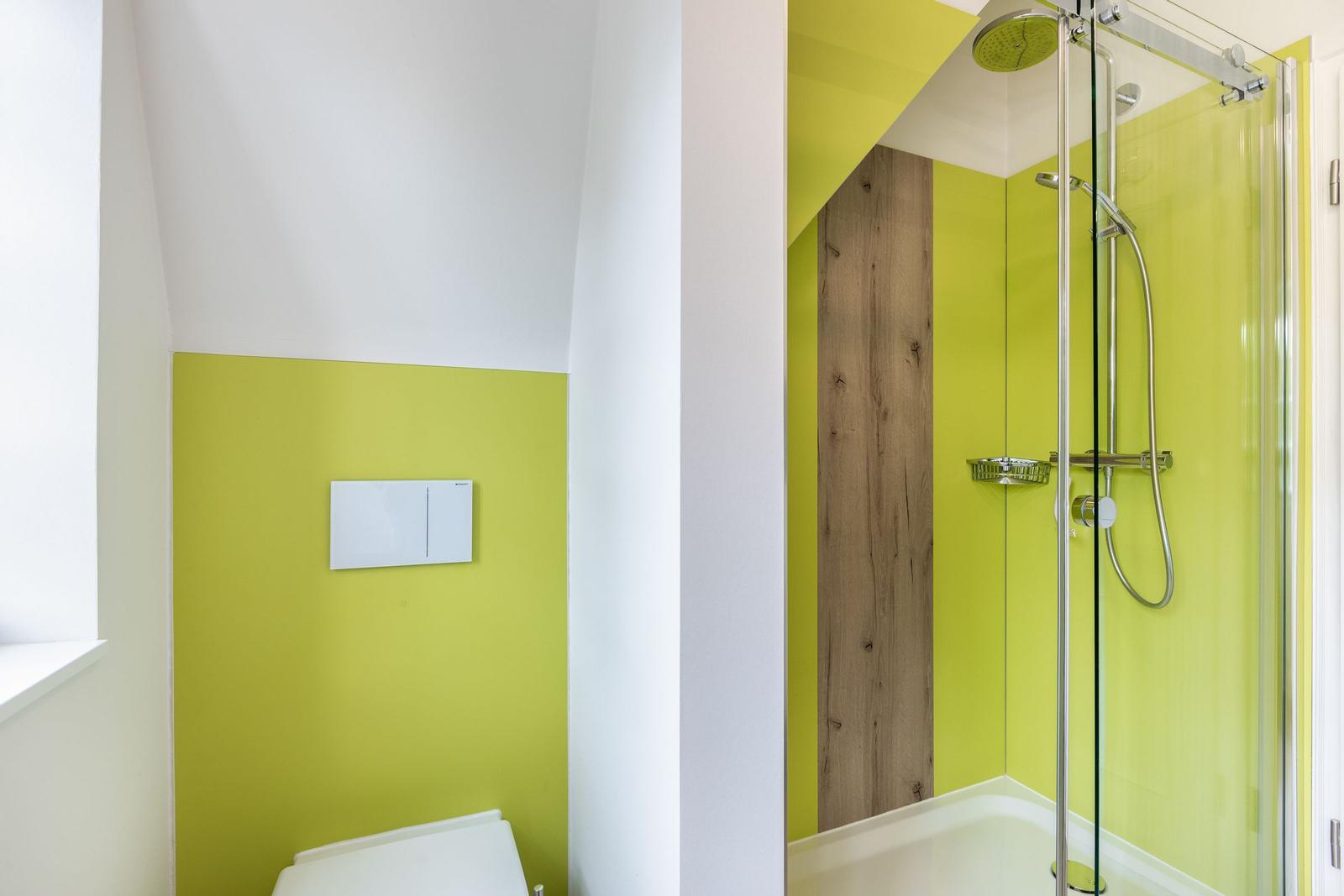 Badezimmer mit Dusche und Toilette, leuchtend grüne Wände und Holzelement.