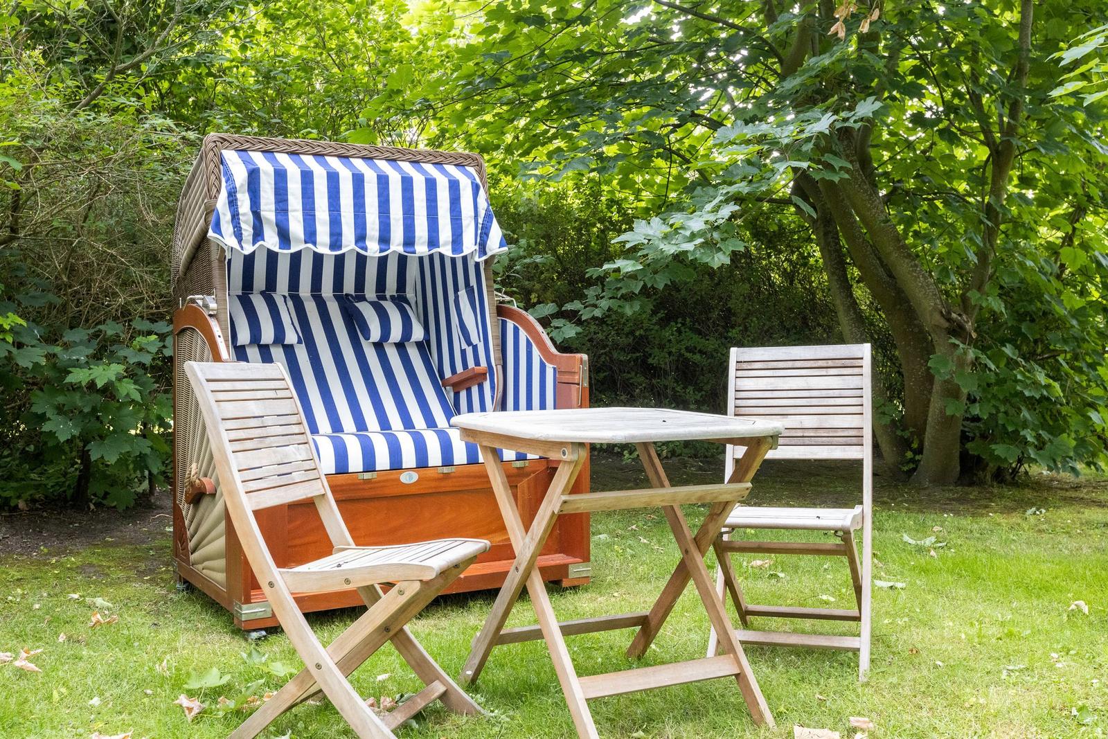 Hochwertige Strandkörbe mit blau-weißem Streifenmuster und Holzstühlen auf grünem Rasen.