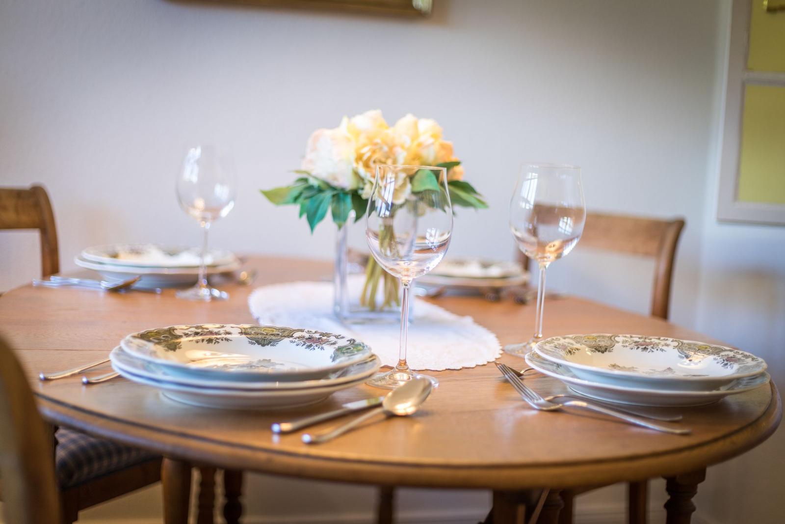 Round wooden table set with plates, glasses, and flower arrangement.
