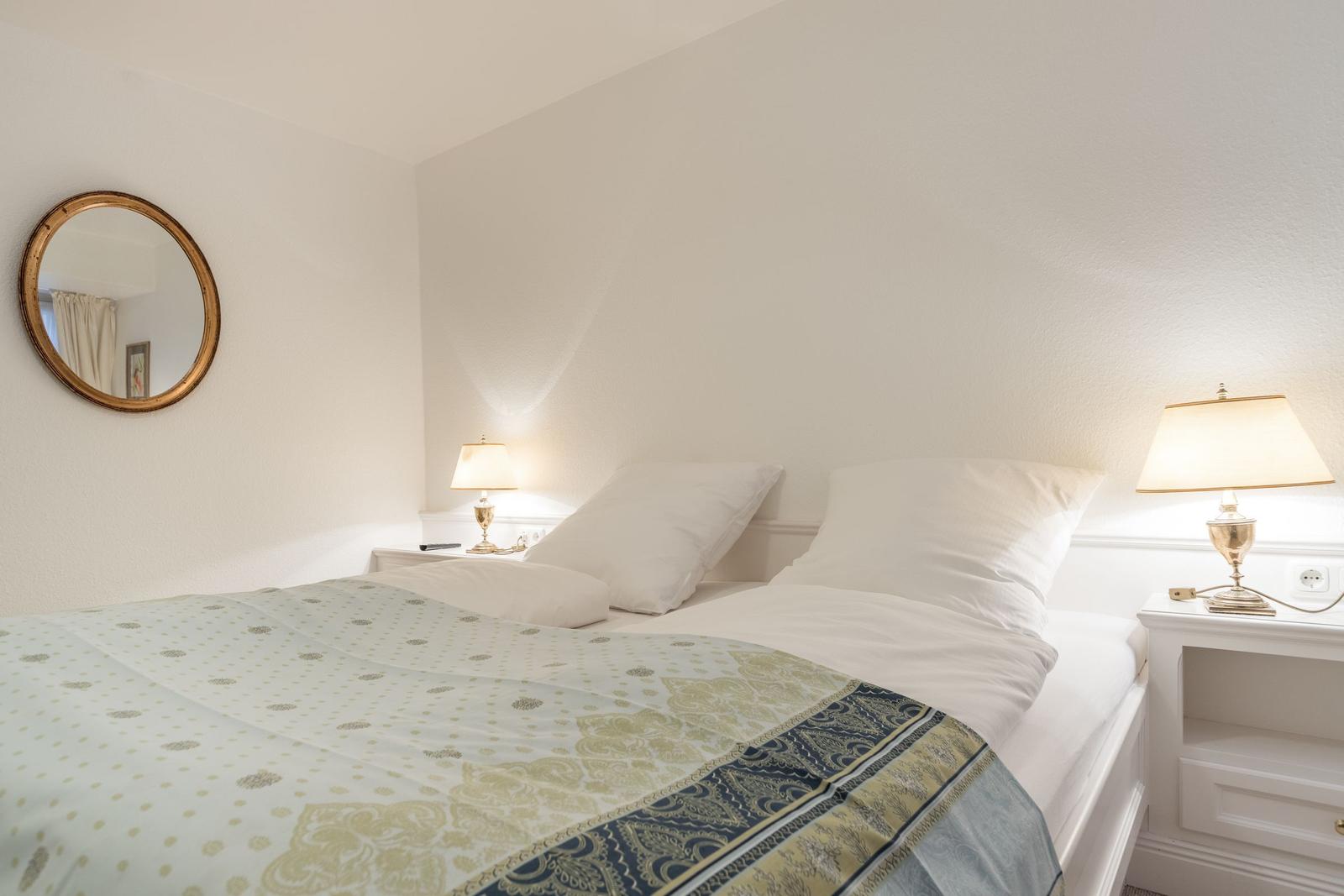 Bedroom with bed, two nightstands and lamps. A round mirror hangs on the wall.