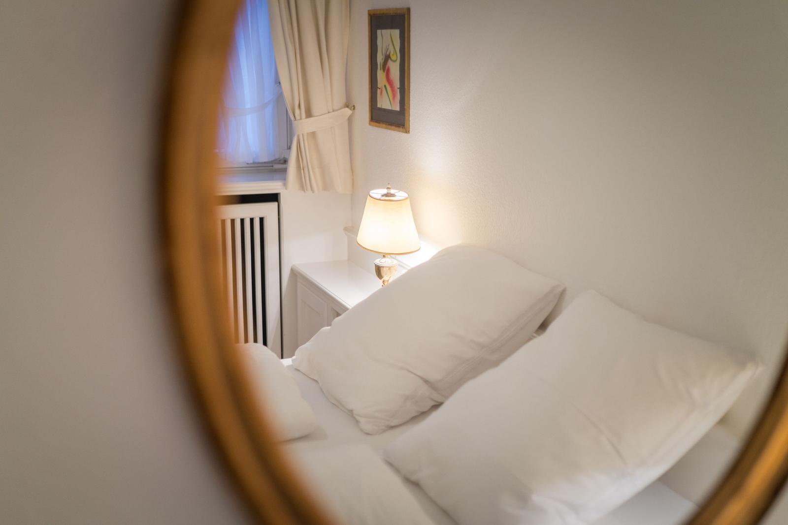 Bedroom with bed, nightstand, and lamp. Window with curtains and wall art.