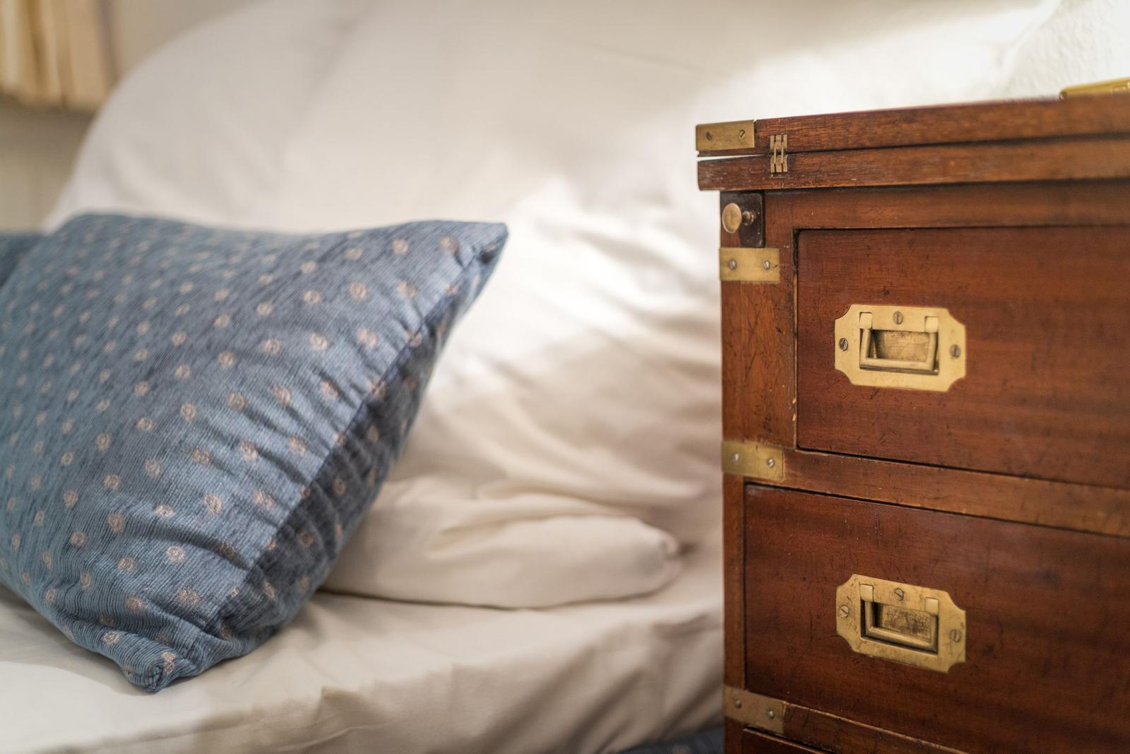 Bed headboard with pillow and wooden chest with two drawers.