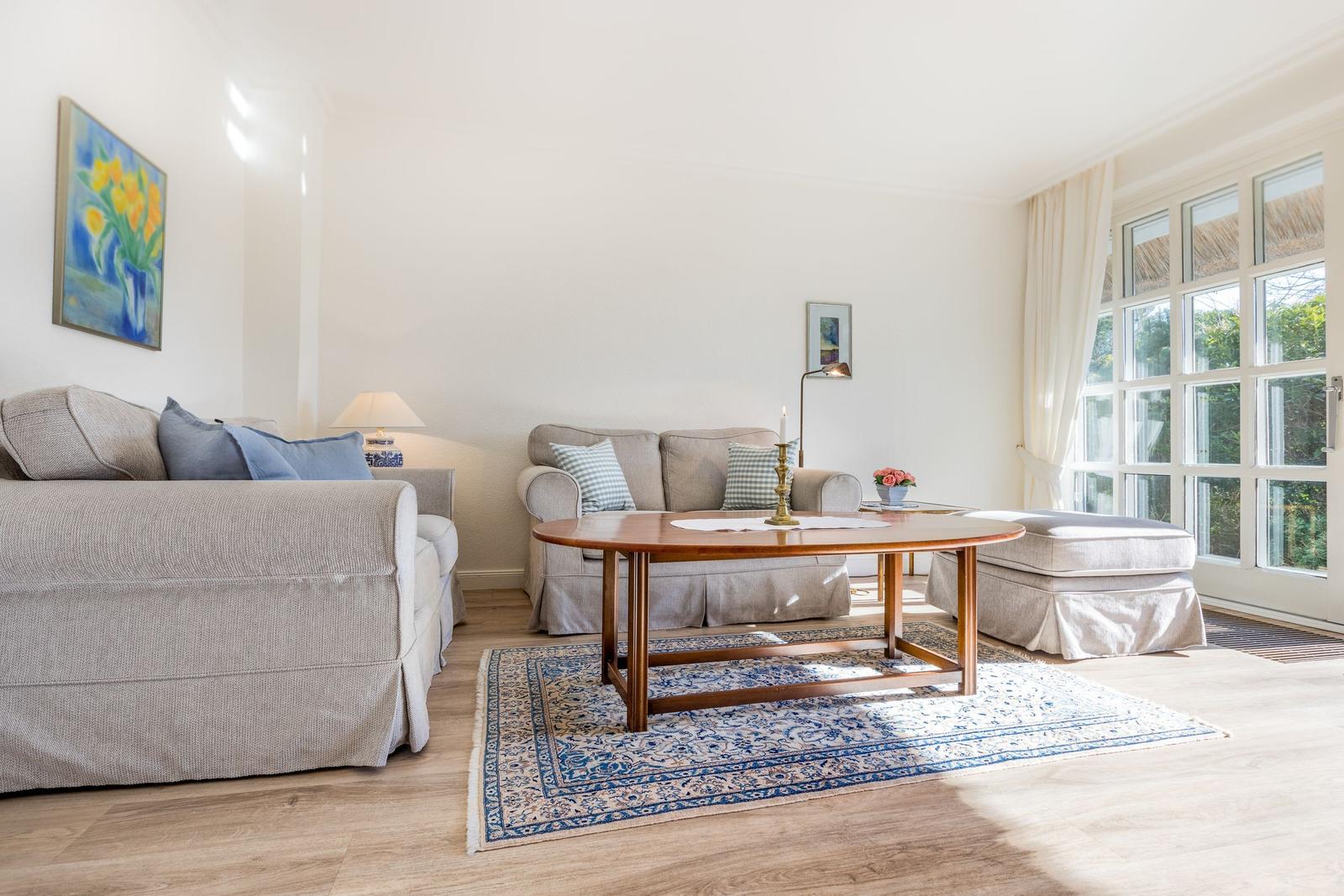 Living room with sofa, coffee table, and windows. Blue rug and wall art.