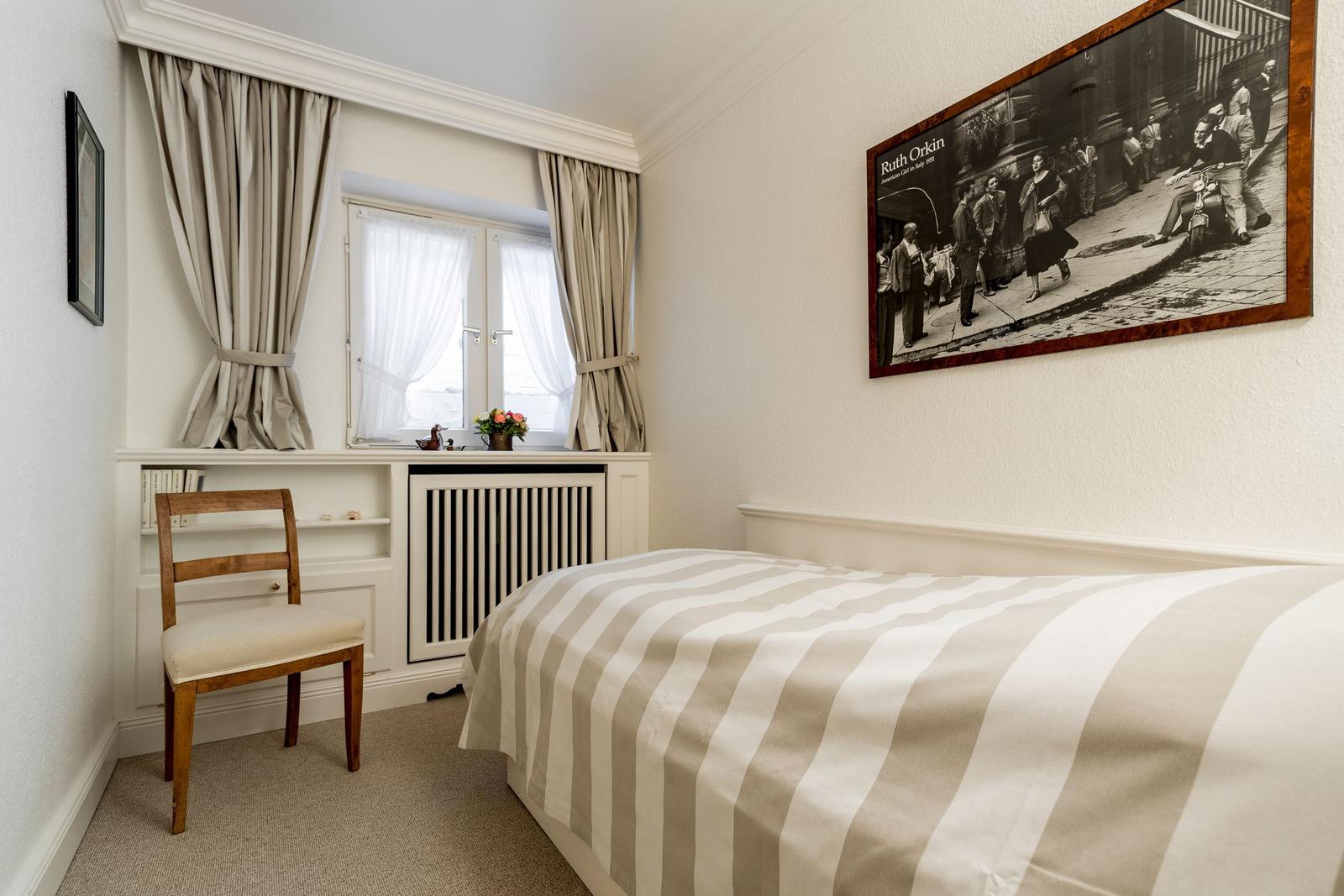 A bedroom with bed, chair, and window. A large photo hangs on the wall.