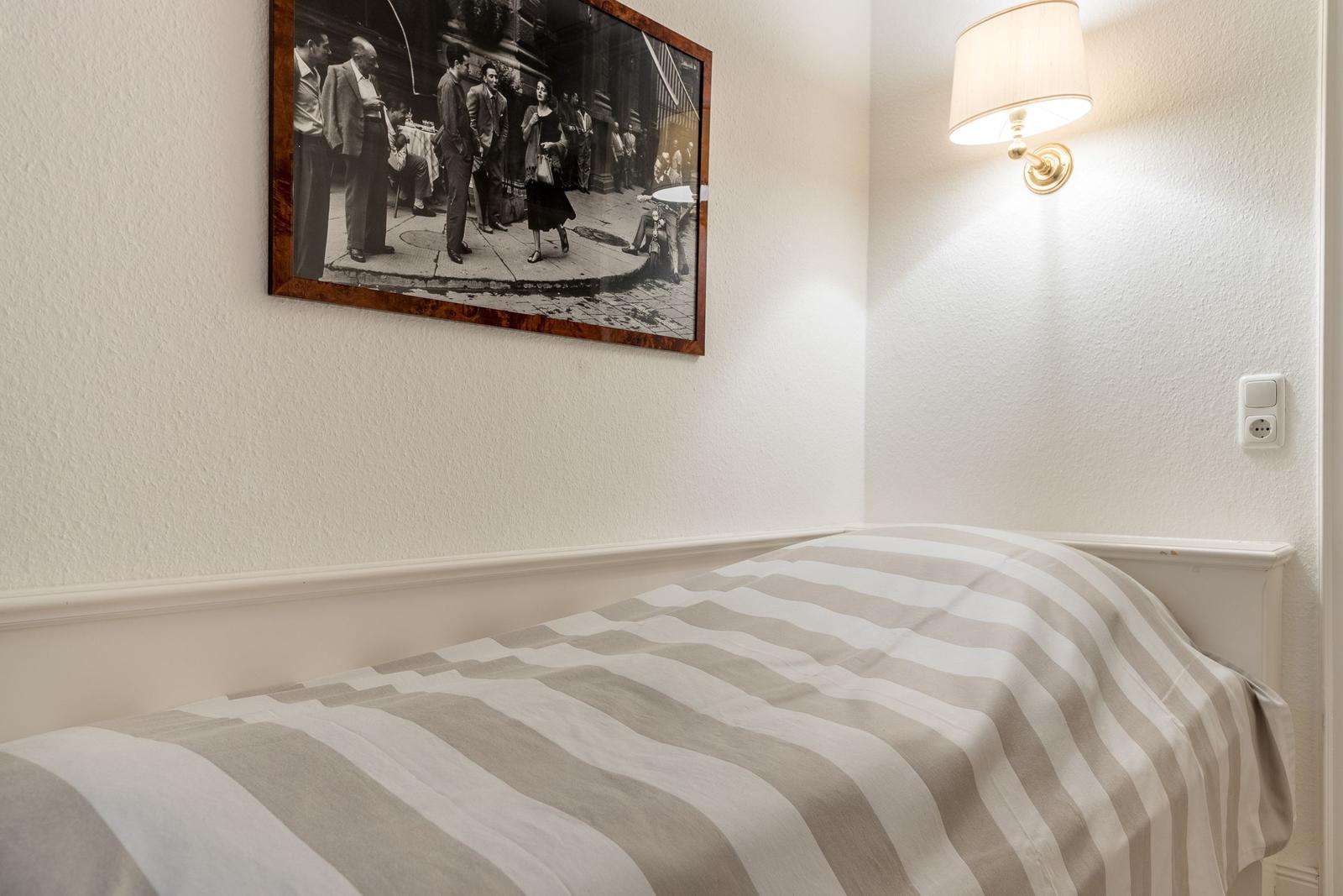 A bed with striped bedding, wall art, and wall lamp.