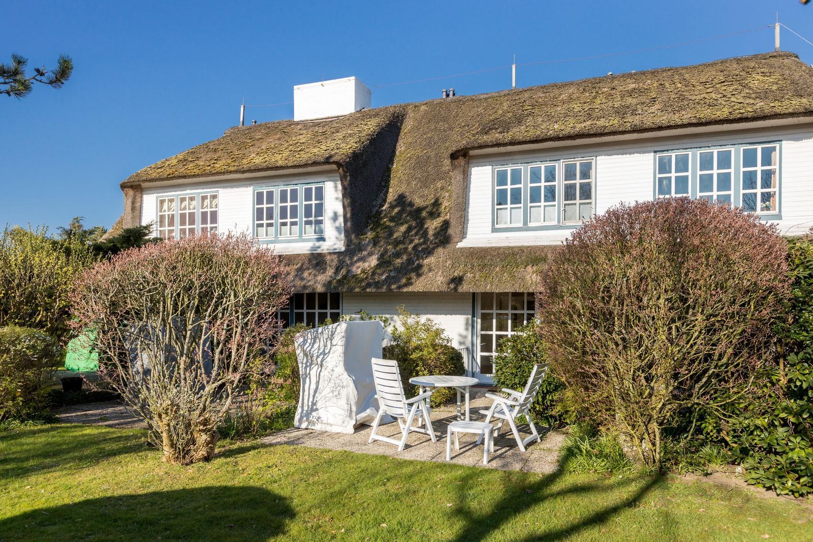 House with thatched roof, white facade, and garden with white outdoor furniture.