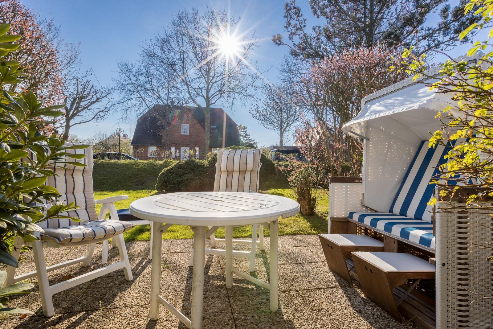 Terrace with table, chairs, and beach cabana under sun.