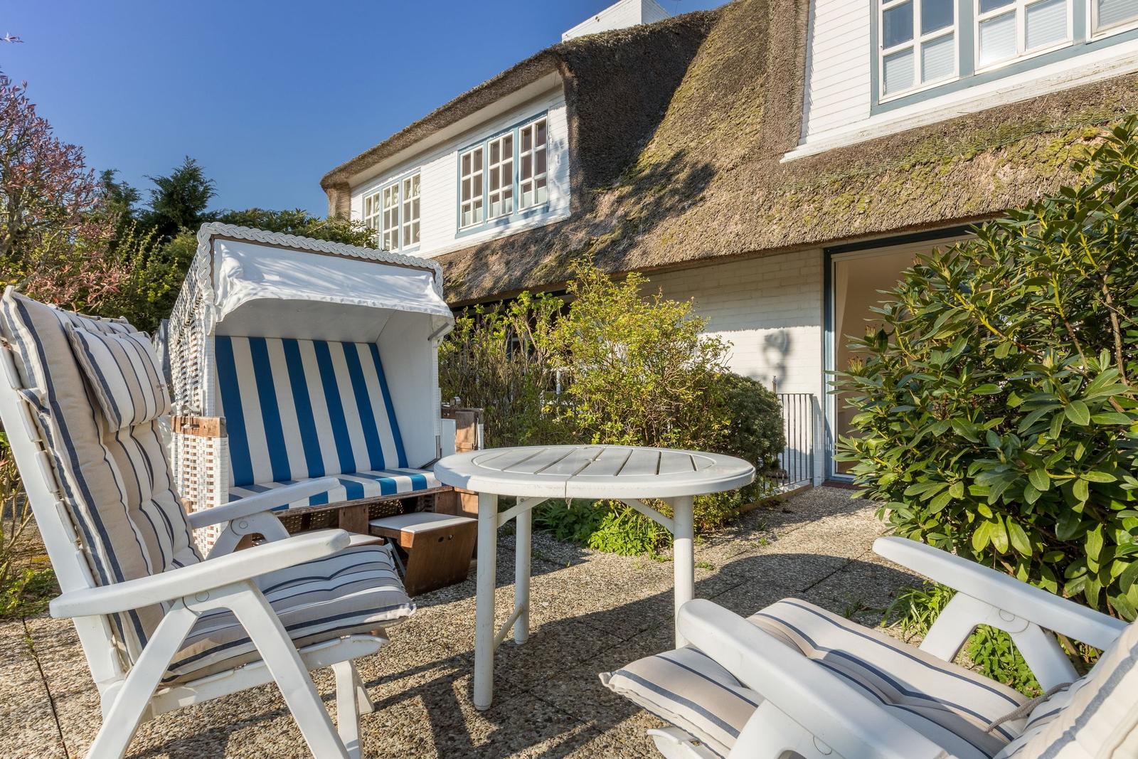 Terrace with lounge chairs and beach cabana in front of a thatched-roof house.