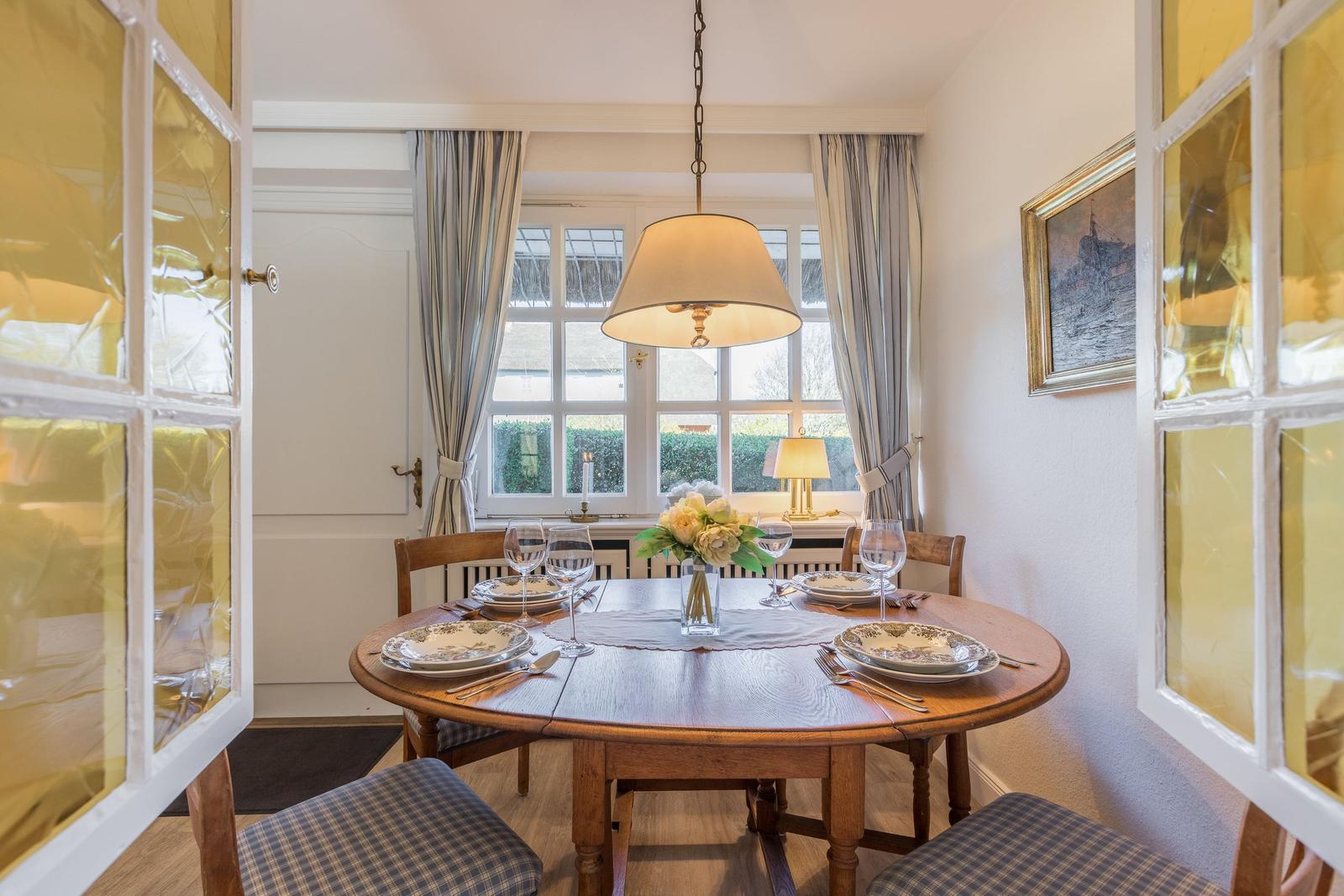 Round wooden table with chairs and table setting in front of window with curtains.
