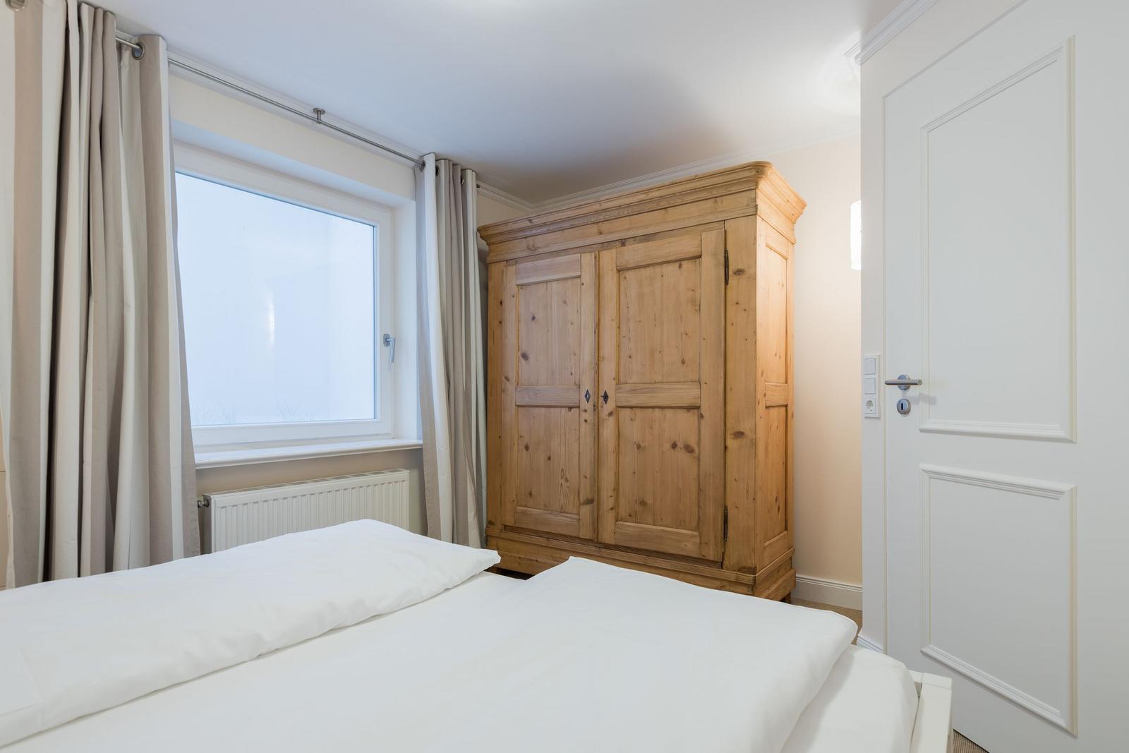 Bedroom with bed, wooden wardrobe, and window with curtains.