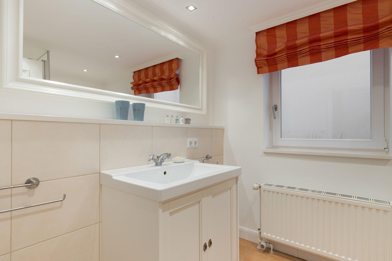 Bathroom with sink, mirror, and window with orange roller blind.