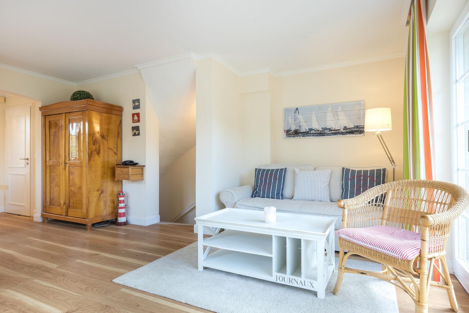 Living room with sofa, wicker chair, and wooden wardrobe. Wall art with sailboats.