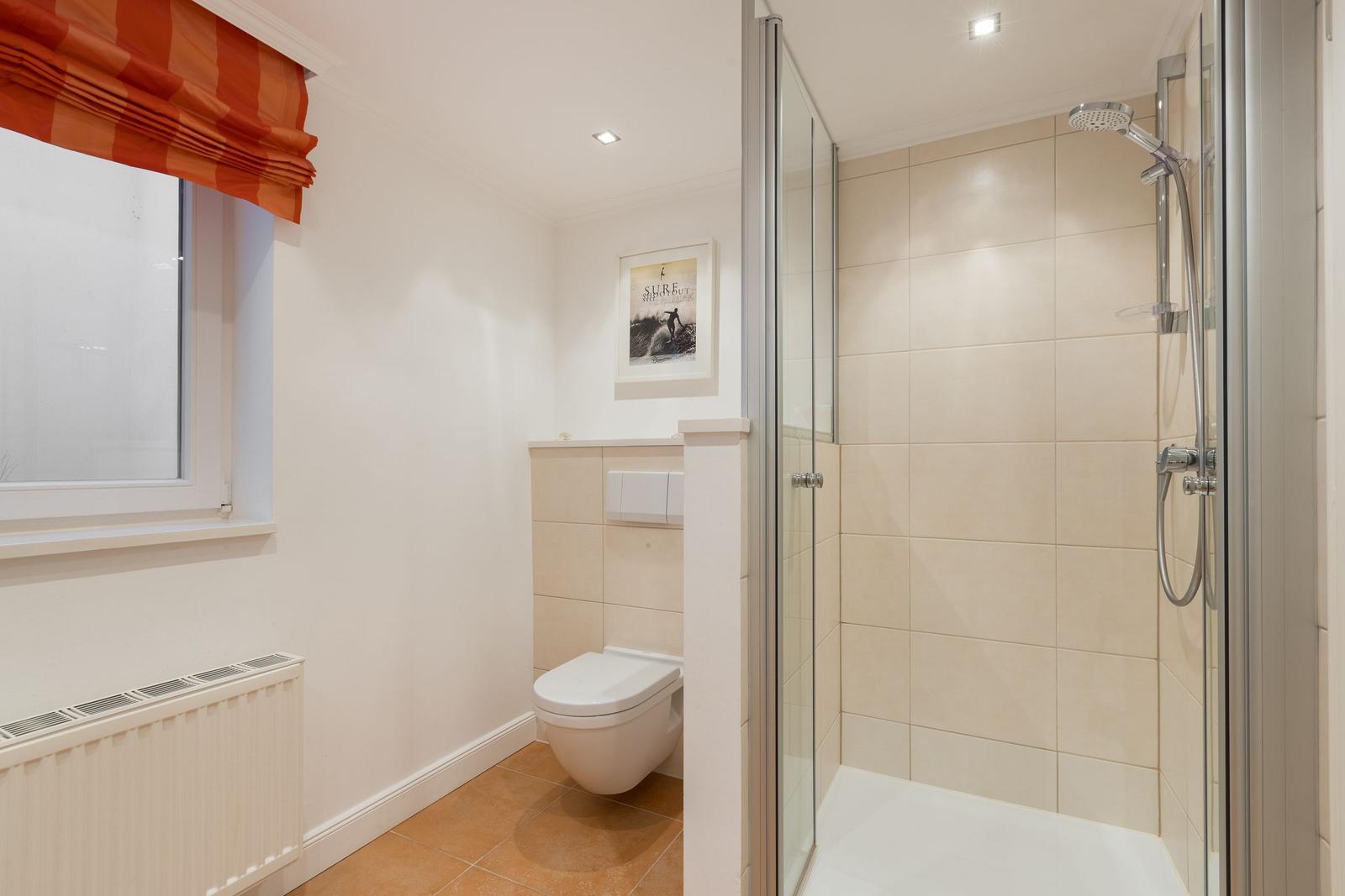 Bath with shower, toilet, and window with orange roller blind.