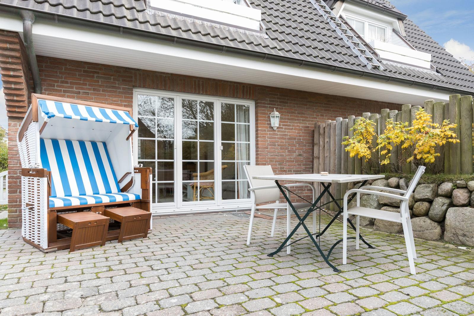 Terrace with beach chair, table and chairs in front of a house with brick wall.
