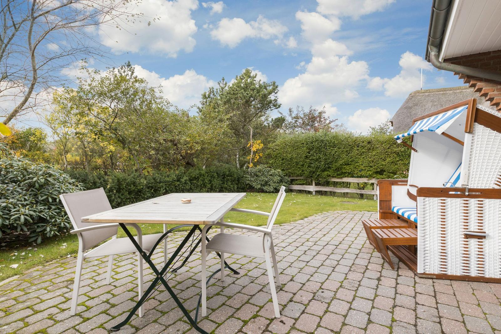Terrace with table, chairs, and beach chair. Background: greenery and sky.