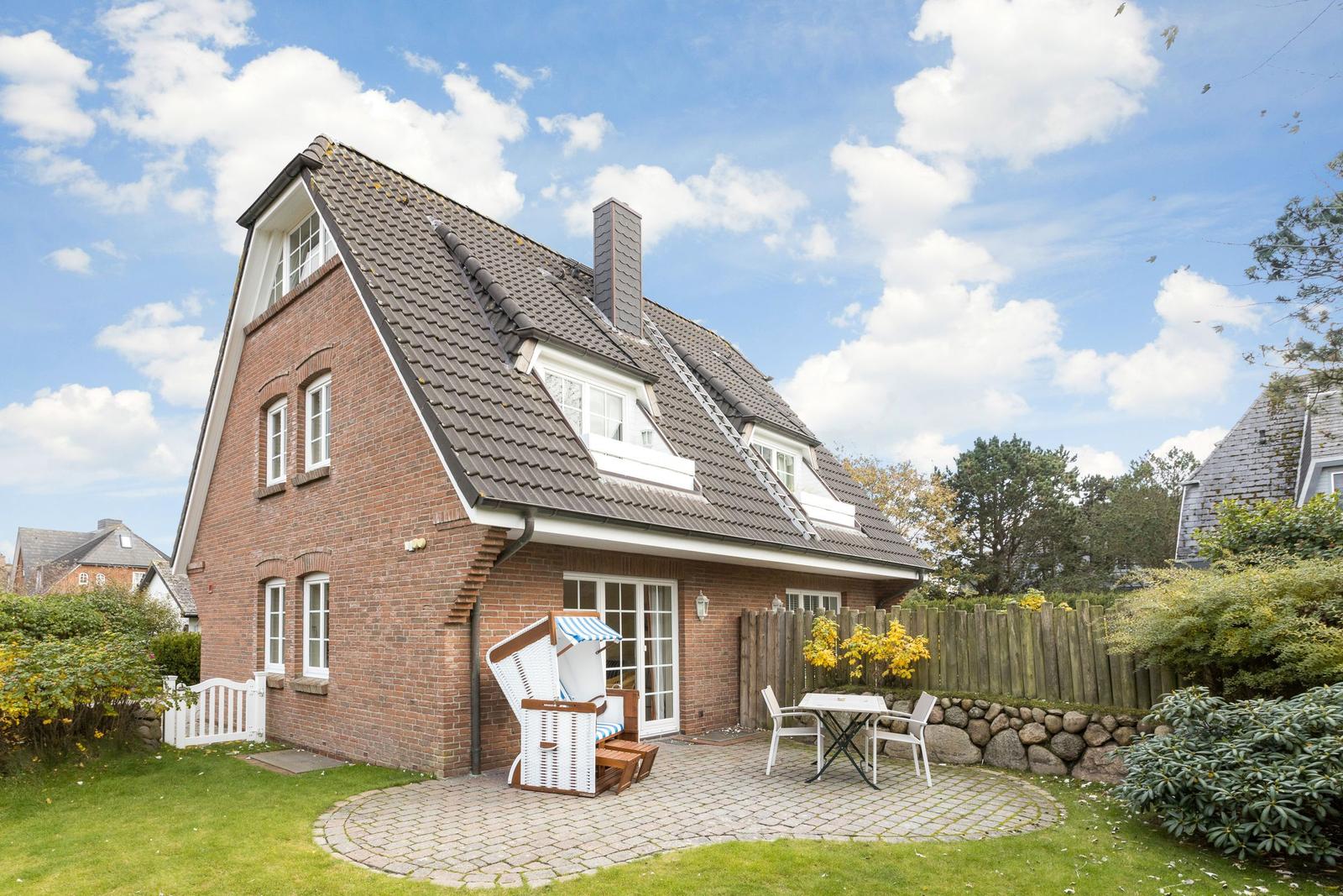 House with garden, terrace, and beach chair. White windows and brick wall.